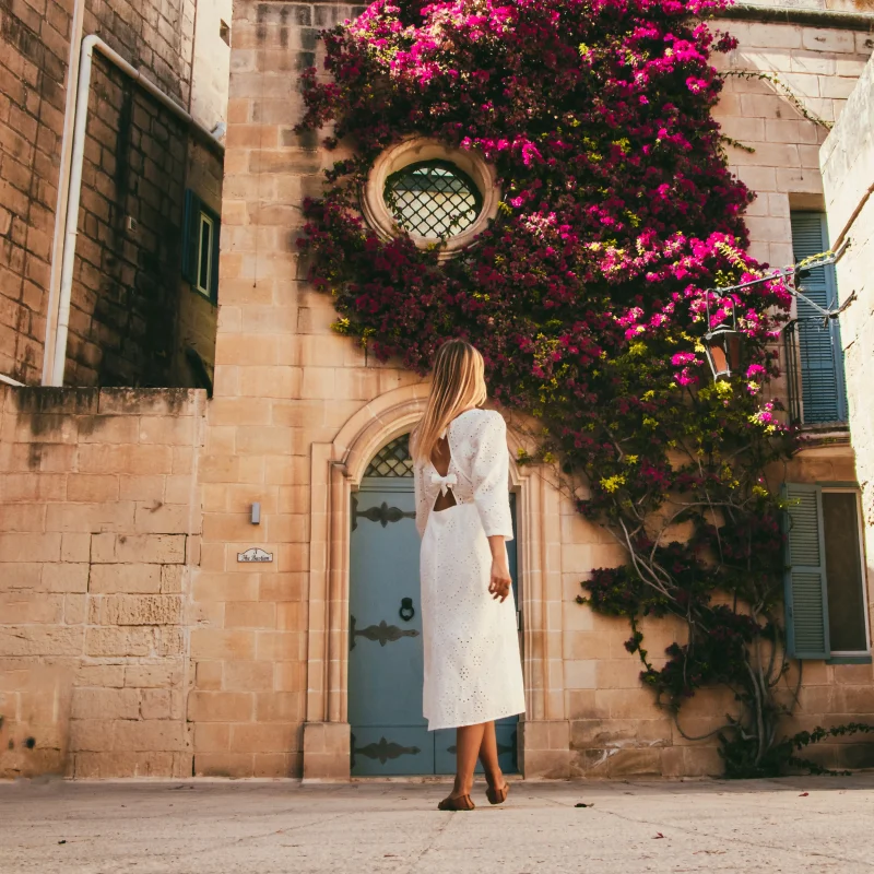 A woman posing in front of a famous Maltese facade covered in bougainvillea vines. This door is found in Mdina and is a famous Malta holiday destination for pictures.