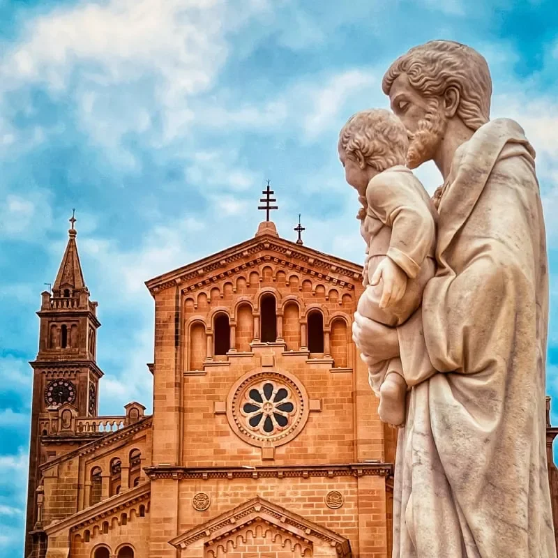 An artistic shot of Ta Pinu's Basilica in Gozo, also capturing an outdoor statue in the foreground.