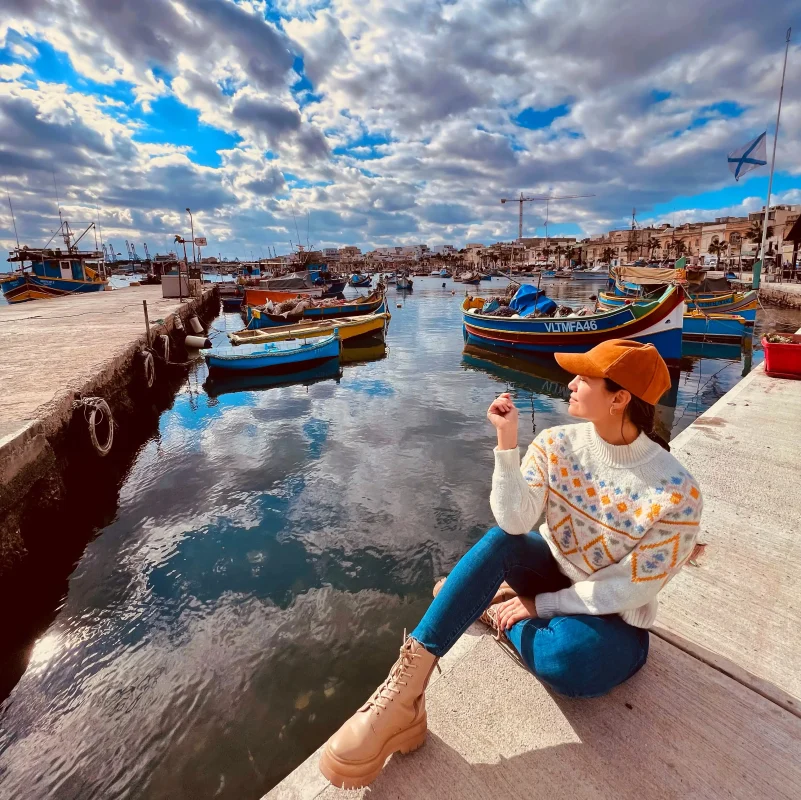 A woman enjoy the sun in Marsaxlokk, overlooking traditional Luzzu boats.
